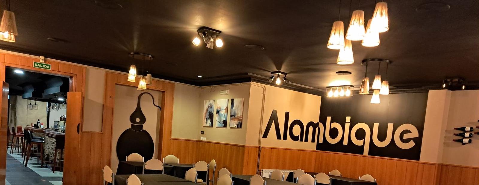 Comedor de O Alambique con lámparas cálidas y el nombre del local en la pared